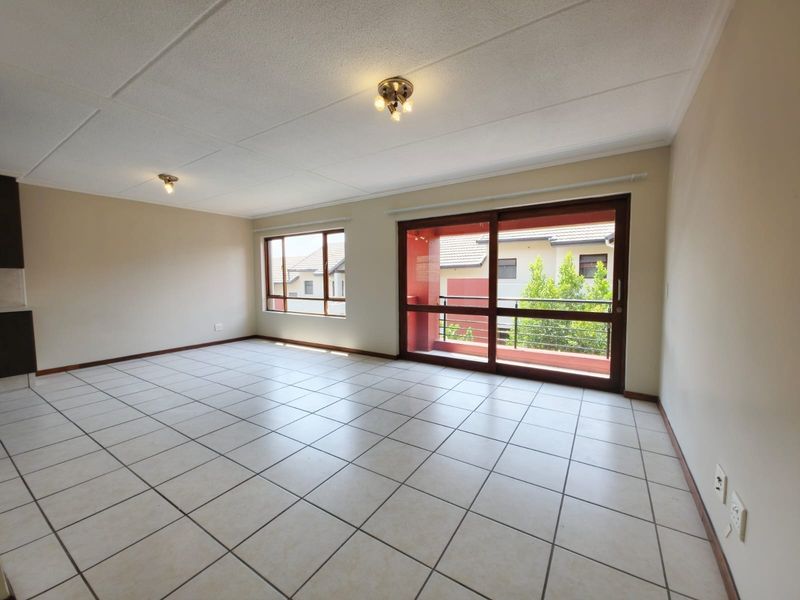 Spacious, empty living area featuring neutral tiled flooring, large windows, and a sliding door leading to a balcony, offering a bright and versatile space.