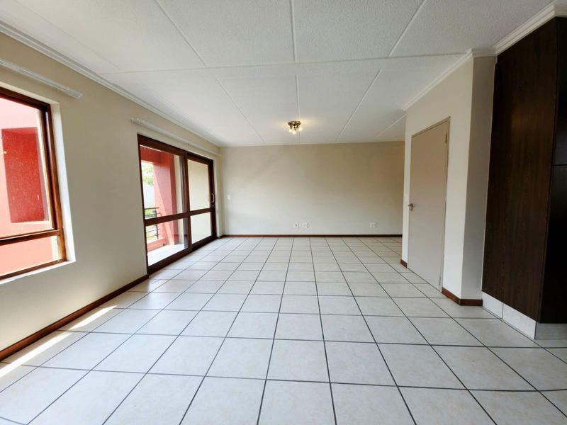 A spacious, empty living area featuring neutral tiled flooring, a sliding glass door leading to a balcony, and a built-in storage cupboard.