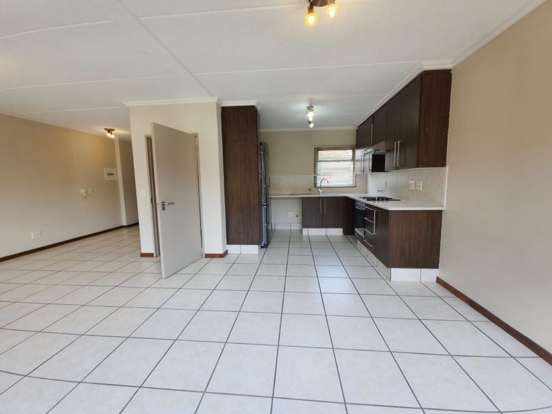 An open-plan kitchen and living area featuring dark wood cabinetry, tiled flooring, and built-in cooking appliances in a clean, vacant space.