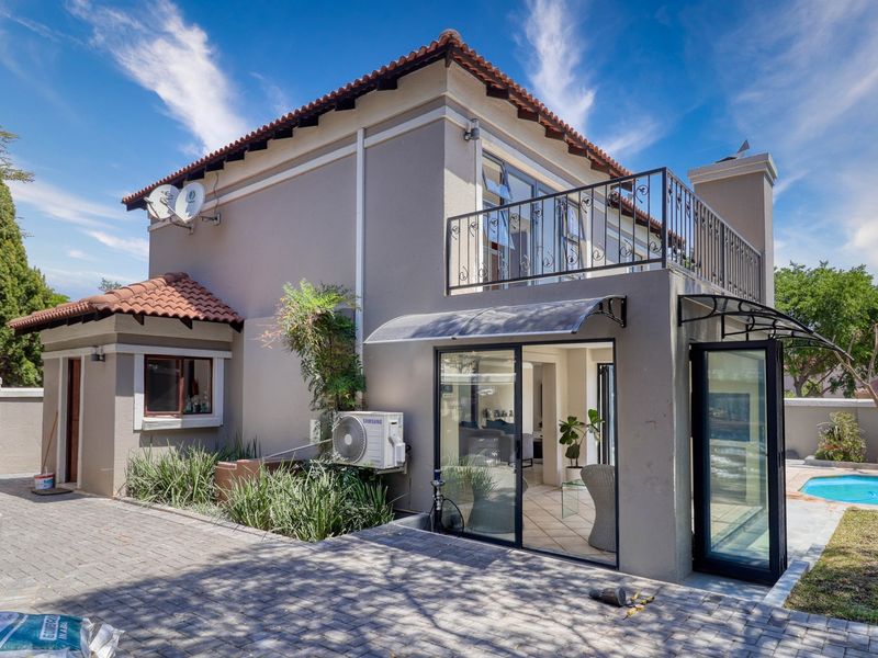 Rear view of a two-story house featuring a paved patio, swimming pool, upper-level balcony with wrought iron railing, and sliding glass doors.