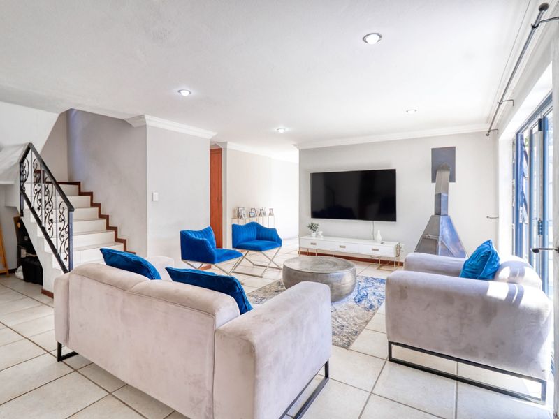 Spacious living room featuring tiled flooring, a modern freestanding fireplace, recessed lighting, and a staircase with a decorative wrought iron balustrade.