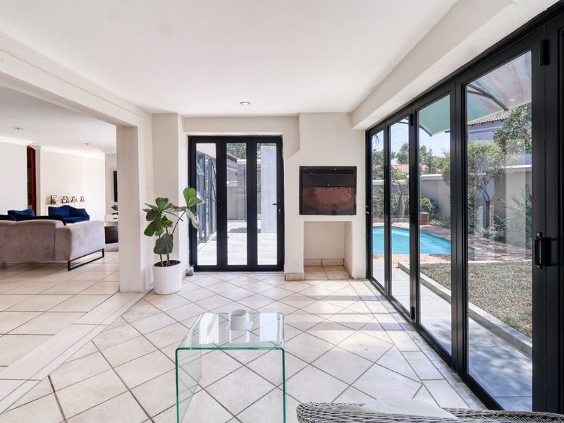 A bright, enclosed patio area featuring tiled flooring, a built-in fireplace, and black aluminium stacker doors opening to the pool and garden.
