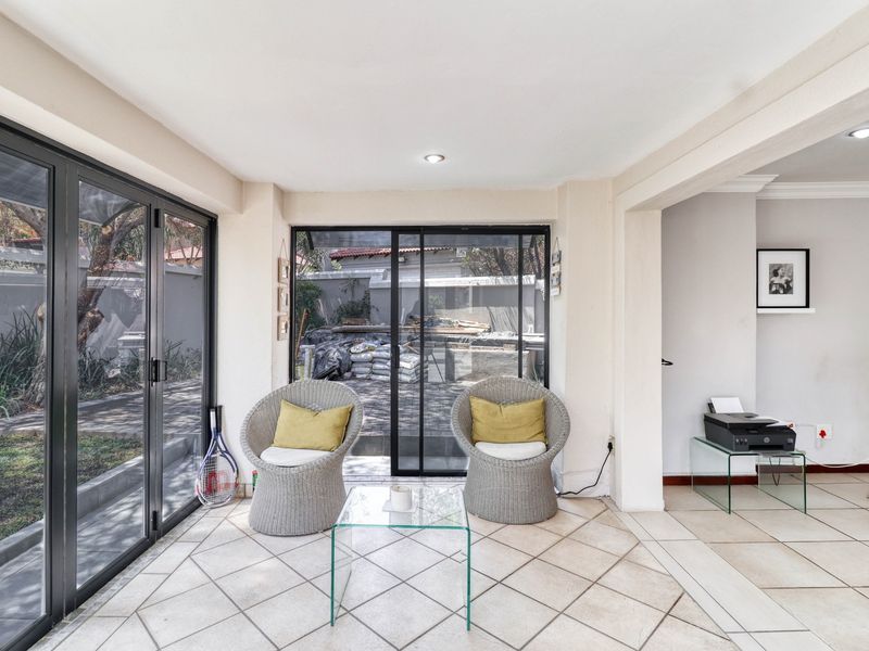 A bright, enclosed patio area featuring tiled flooring, recessed lighting, and large aluminium sliding and folding doors providing access to the garden.