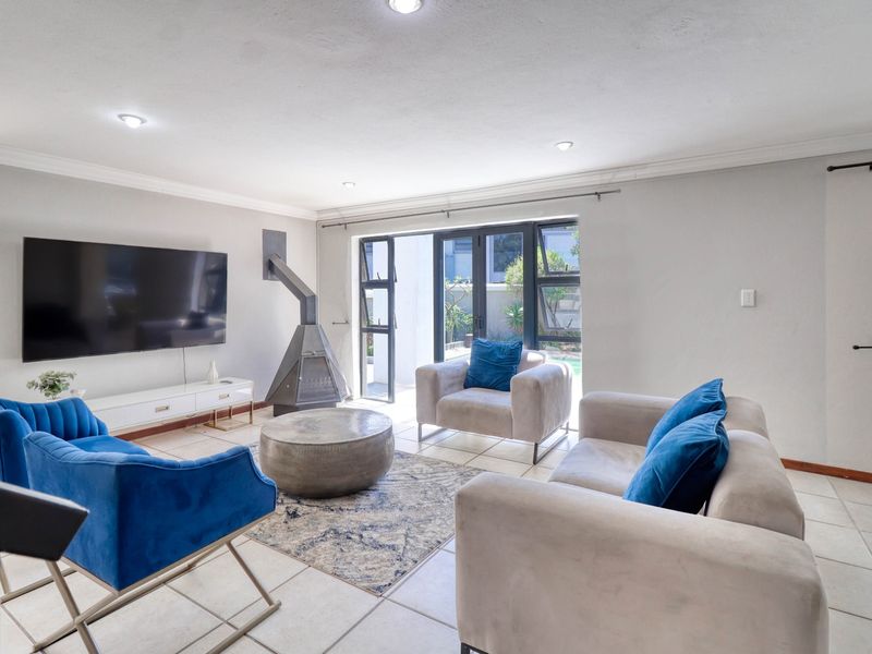 A bright and modern living room featuring tiled floors, a contemporary freestanding fireplace, and large glass doors providing seamless access to the outdoor area.