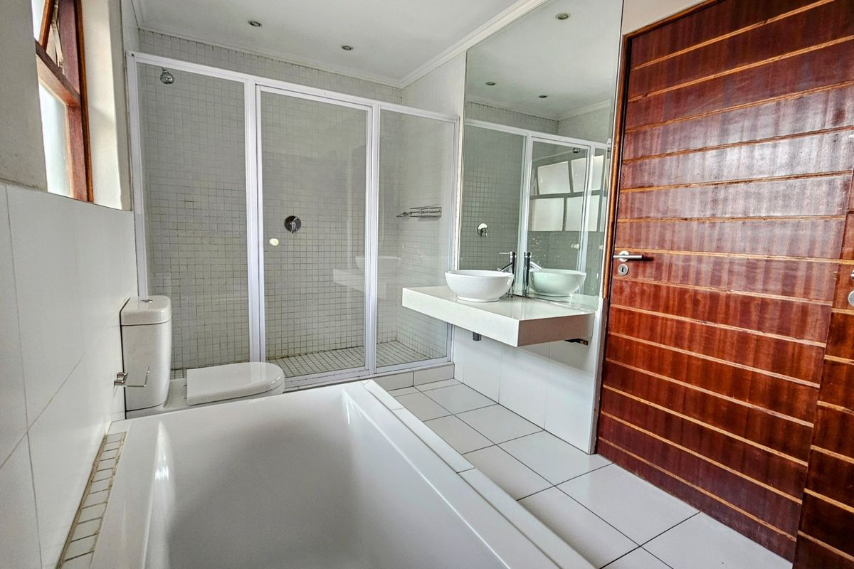 A functional bathroom featuring a built-in bathtub, a separate shower enclosure, a wall-mounted basin with a vessel sink, and tiled finishes.
