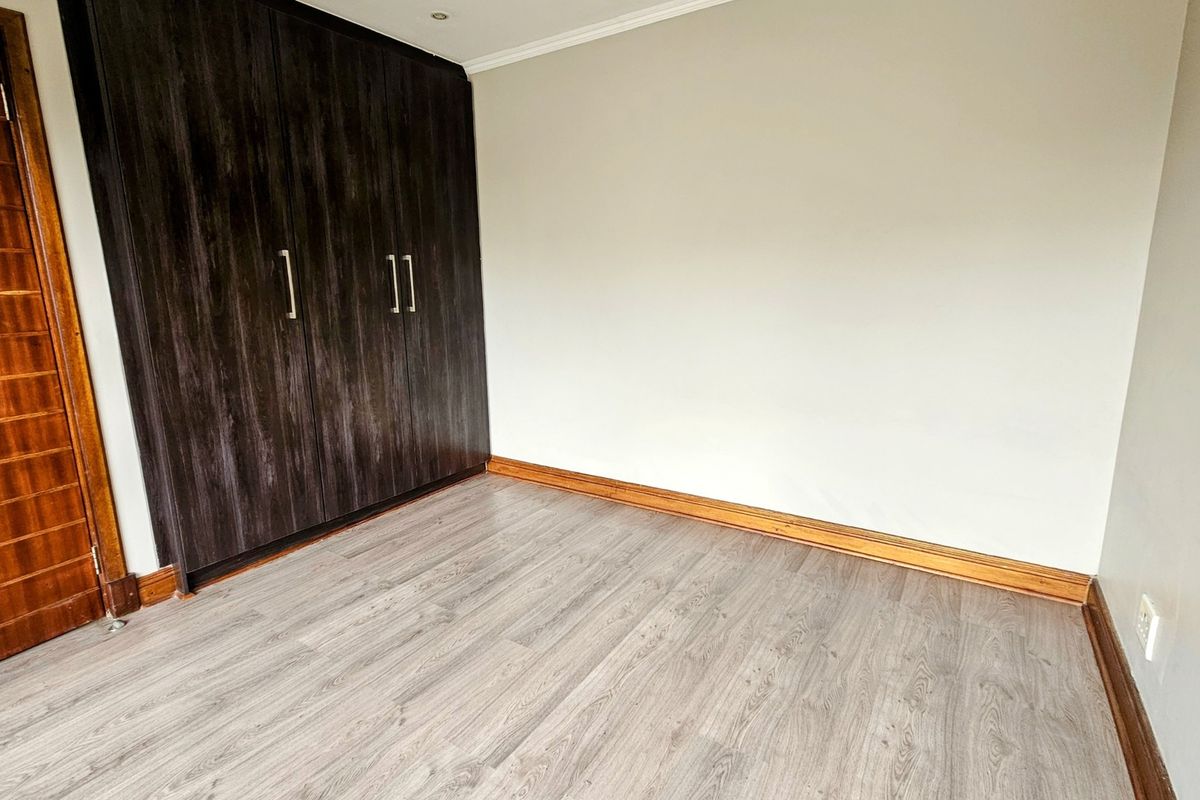 A clean, empty bedroom featuring modern laminate flooring, neutral walls, and dark wood-finish built-in cupboards.