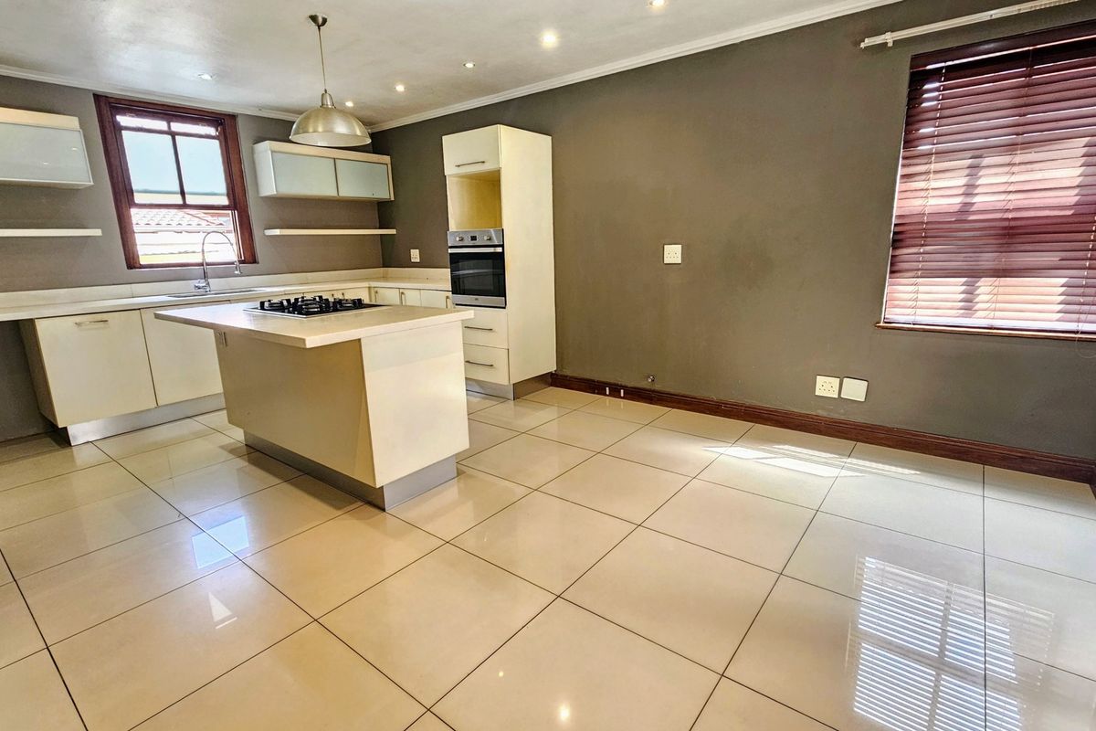 A spacious, modern kitchen featuring a central island with a gas hob, built-in oven, ample cabinetry, and neutral tiled flooring.