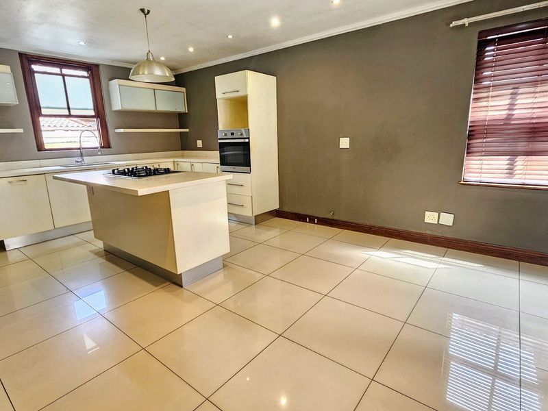 A spacious, modern kitchen featuring a central island with a gas hob, built-in oven, ample cabinetry, and neutral tiled flooring.
