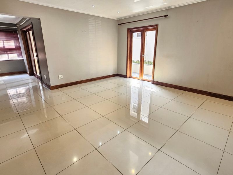 A spacious, empty living area featuring polished porcelain floor tiles, neutral walls, and double glass doors leading to an outdoor space.