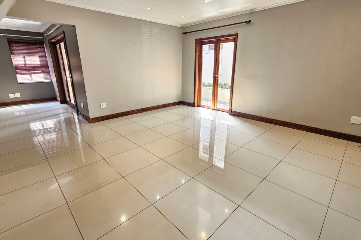 A spacious, empty living area featuring polished porcelain floor tiles, neutral walls, and double glass doors leading to an outdoor space.