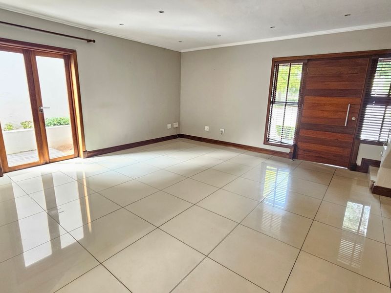 Spacious, light-filled living area featuring polished porcelain tiles, recessed lighting, and direct access to the exterior through wooden french doors.
