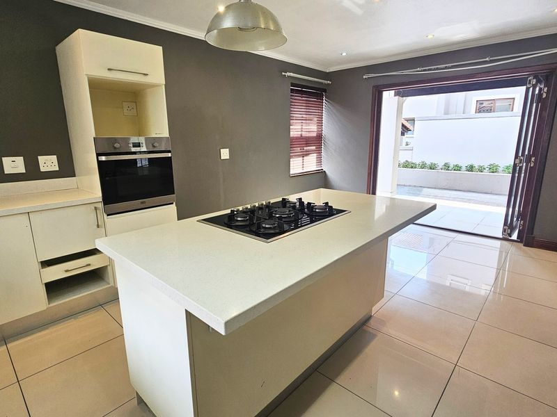 Modern kitchen featuring a central island with a gas hob, built-in oven, stone countertops, and direct access to an outdoor patio area.