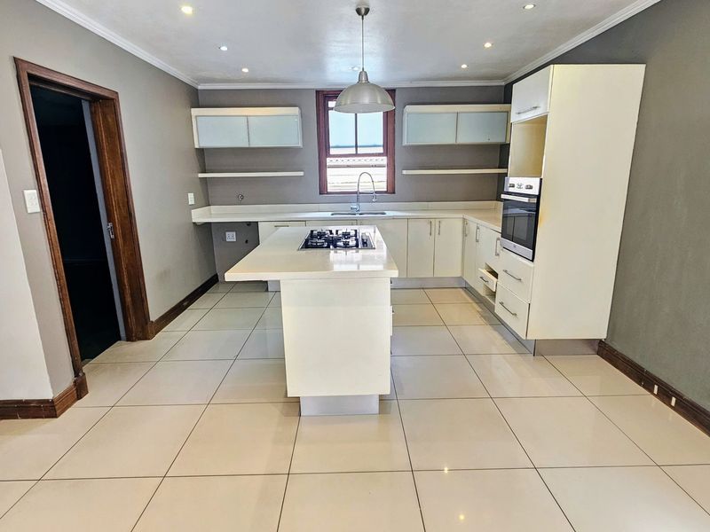 A spacious, empty kitchen featuring a central island with a gas hob, built-in oven, ample cabinetry, and neutral tiled flooring.