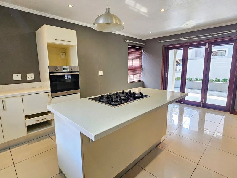 Modern kitchen featuring a central island with a gas hob, built-in oven, stone countertops, and direct access to the patio through glass french doors.