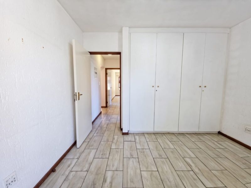 A bright, empty bedroom featuring neutral tiled flooring and ample built-in cupboard storage, leading into a connecting hallway.