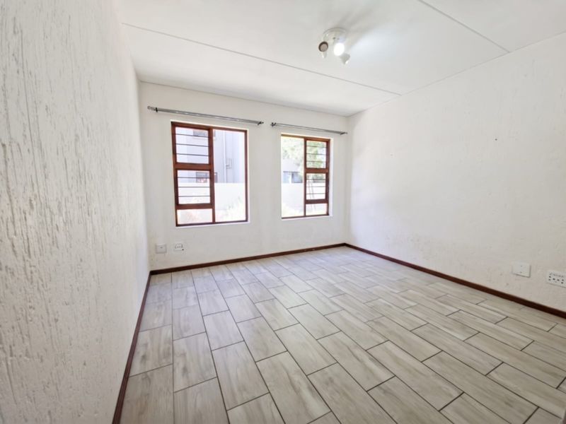 An empty bedroom featuring light-toned tiled flooring, dual steel-framed windows, and textured walls, providing a blank canvas for potential interior design updates.