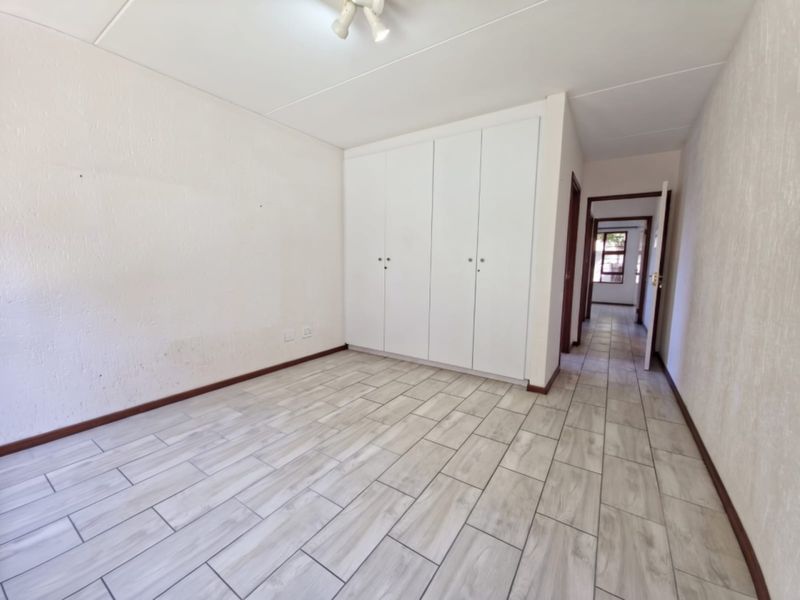 An empty bedroom featuring light-toned tiled flooring, built-in cupboards, and neutral wall finishes, offering a clean and versatile space.