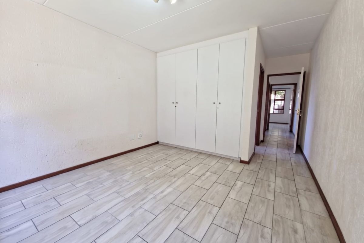 An empty bedroom featuring light-toned tiled flooring, built-in cupboards, and neutral wall finishes, offering a clean and versatile space.
