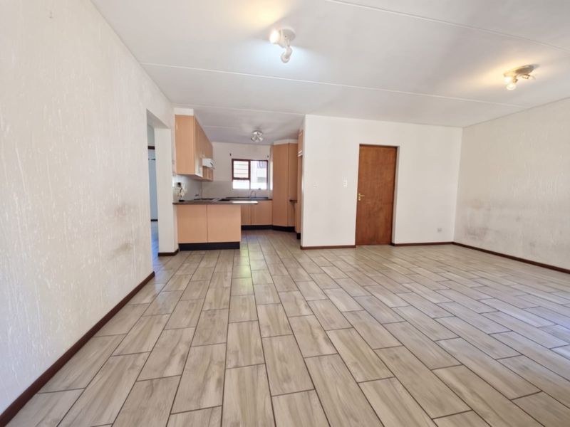An empty open-plan living and kitchen area featuring tiled flooring, built-in cabinetry, and neutral walls, offering a blank canvas for renovation.