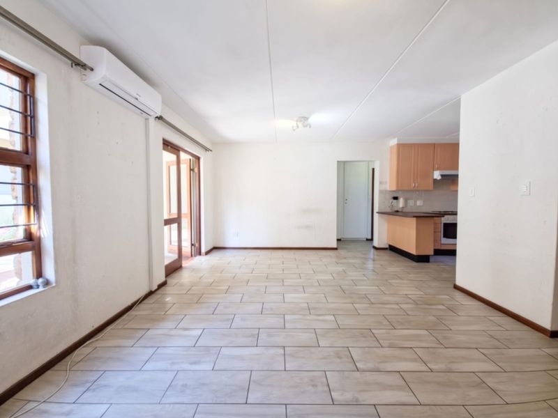 Spacious open-plan living area featuring tiled flooring, an air conditioning unit, and a functional kitchen with built-in cabinetry and appliances.