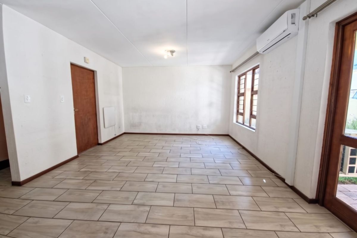 An empty, open-plan living area featuring tiled flooring, an air conditioning unit, and direct access to an outdoor space.