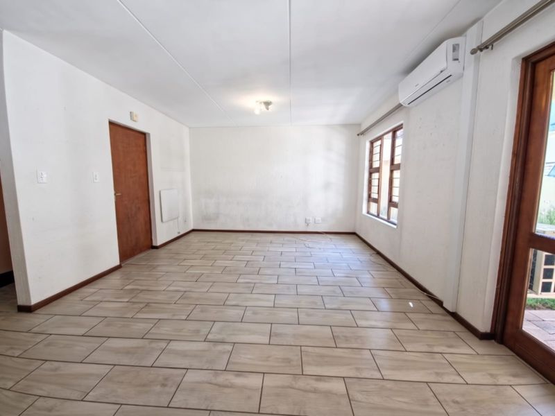 An empty, open-plan living area featuring tiled flooring, an air conditioning unit, and direct access to an outdoor space.