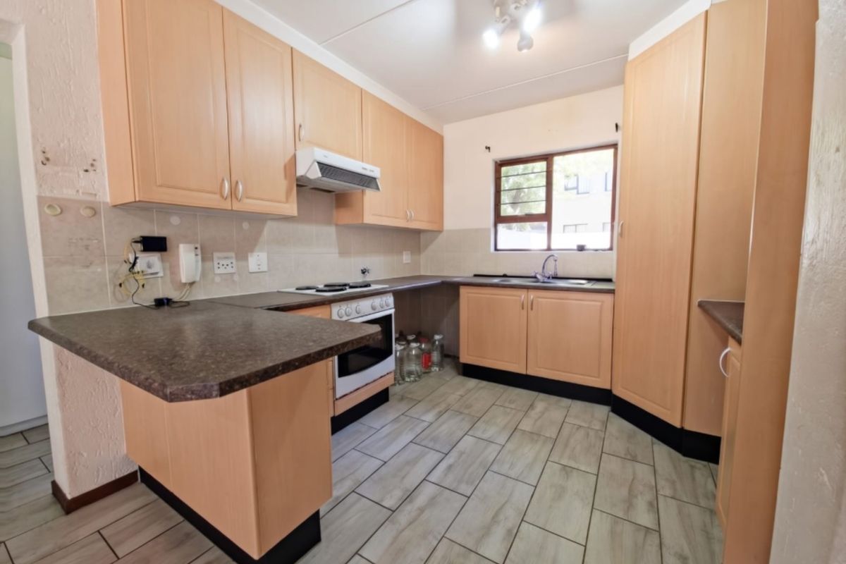 A functional kitchen featuring light wood-tone cabinetry, laminate countertops, built-in oven with extractor, and tiled flooring throughout.