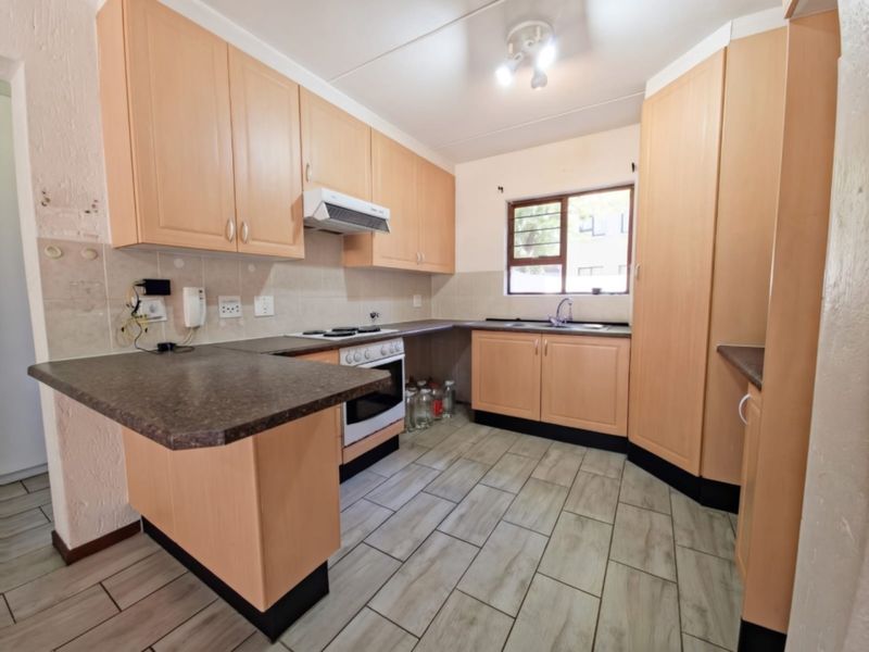 A functional kitchen featuring light wood-tone cabinetry, laminate countertops, built-in oven with extractor, and tiled flooring throughout.