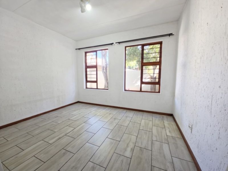 A bright, empty bedroom featuring wood-look tile flooring, timber-framed windows with security bars, and neutral textured walls.