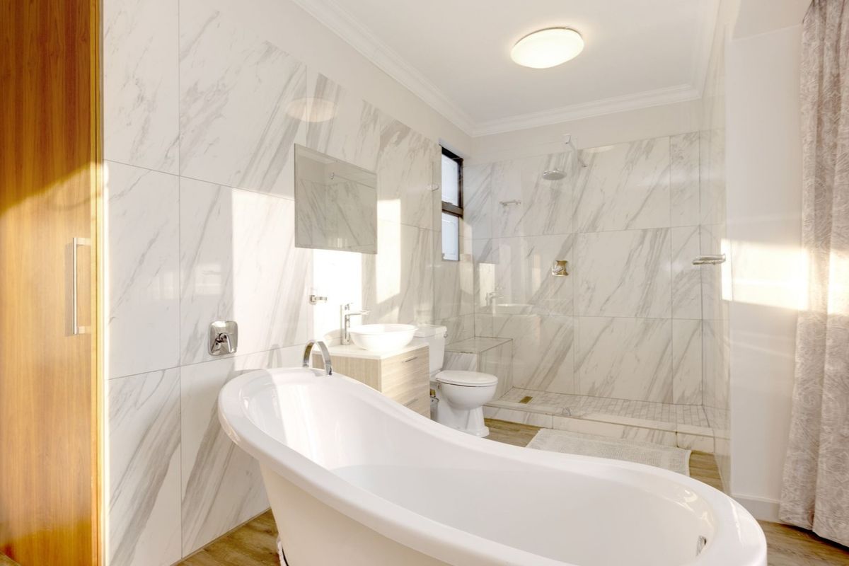Modern bathroom featuring a freestanding bathtub, walk-in shower with glass enclosure, marble-look wall tiling, and a vanity basin.
