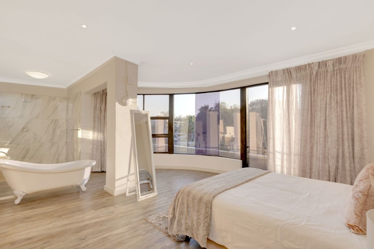 Spacious open-plan bedroom featuring an integrated en-suite bathroom with a freestanding bathtub, large curved windows, and modern wood-look flooring.