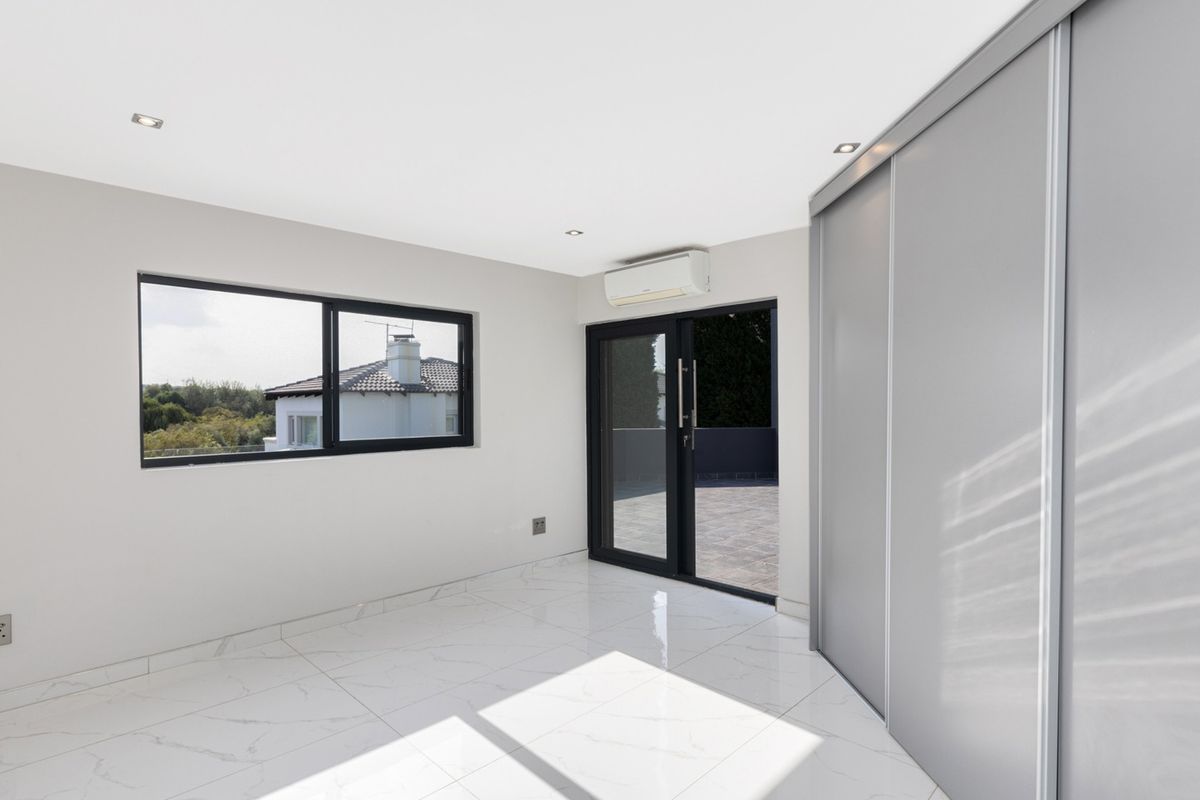 A bright, modern bedroom featuring sleek white marble-look tiled flooring, built-in sliding wardrobes, an air conditioning unit, and direct access to an outdoor balcony.