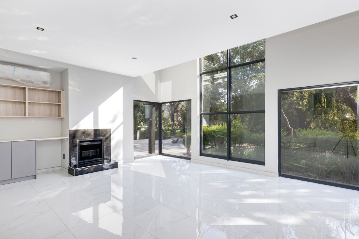 Spacious living area featuring high ceilings, large floor-to-ceiling windows, polished marble-look tile flooring, and a modern built-in fireplace with marble surround.