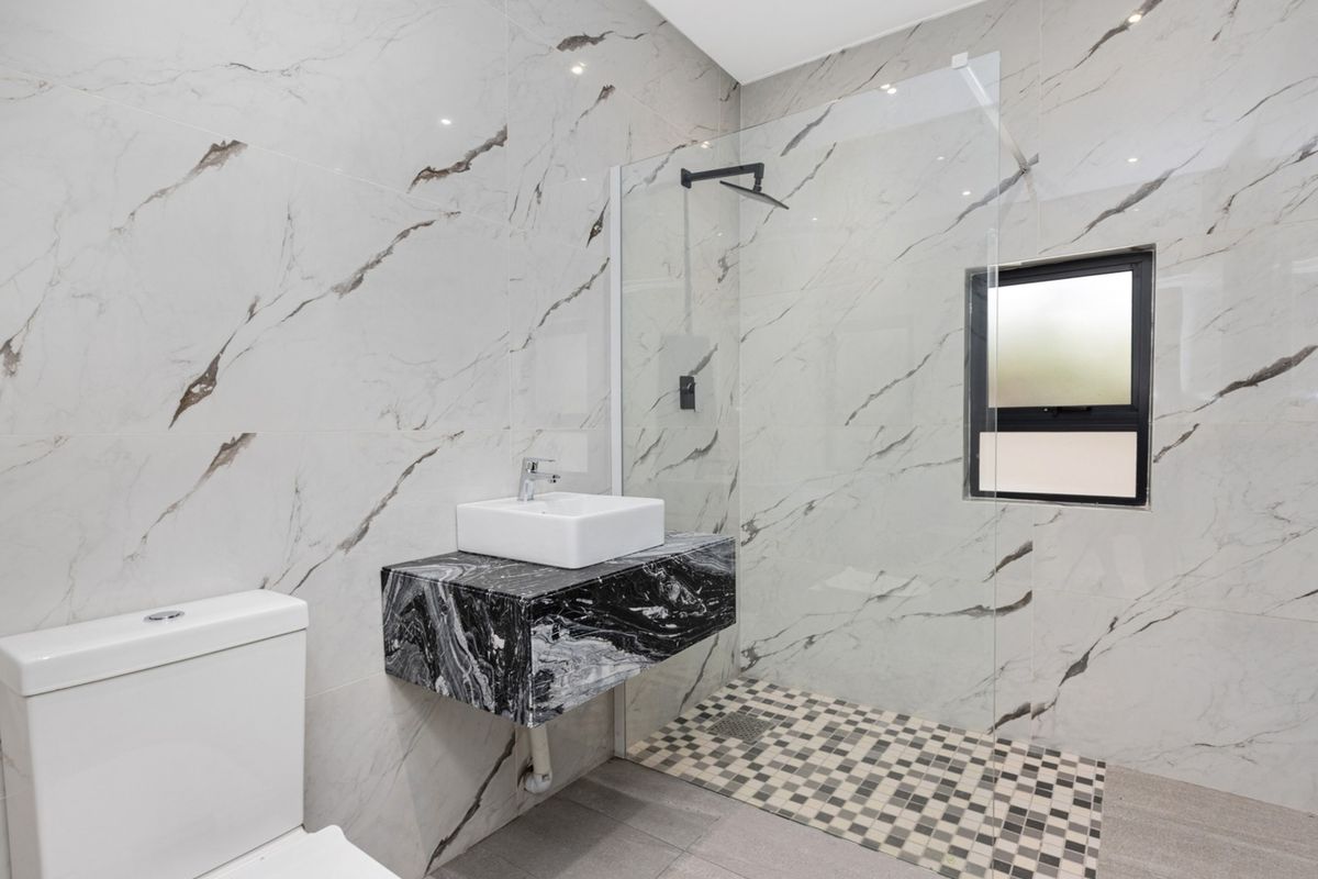 Modern bathroom featuring floor-to-ceiling marble-look wall tiles, a floating black marble vanity with a vessel sink, and a walk-in glass shower enclosure.