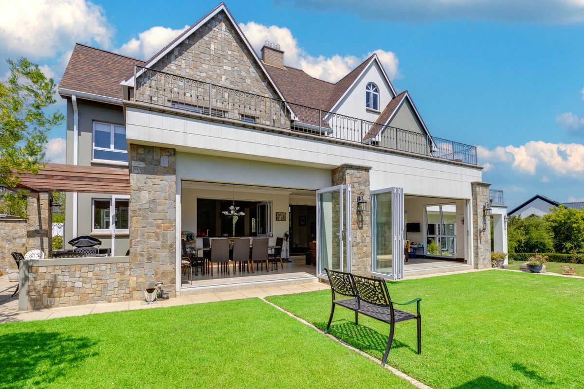 Rear view of a luxury multi-story residence featuring stone facade, expansive bi-fold doors opening to a patio, and an upper-level balcony with iron railings.