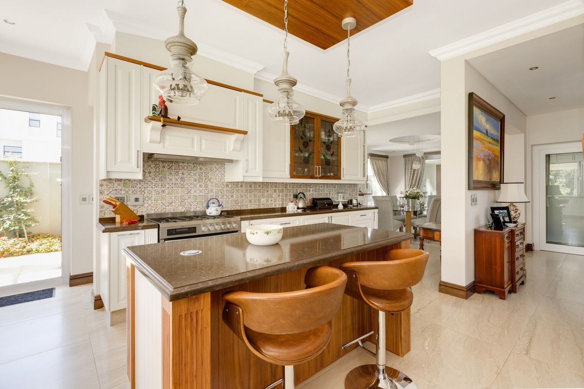 Modern kitchen featuring a central island with stone countertops, gas stove, decorative tiled backsplash, and elegant pendant lighting, flowing into the dining area.