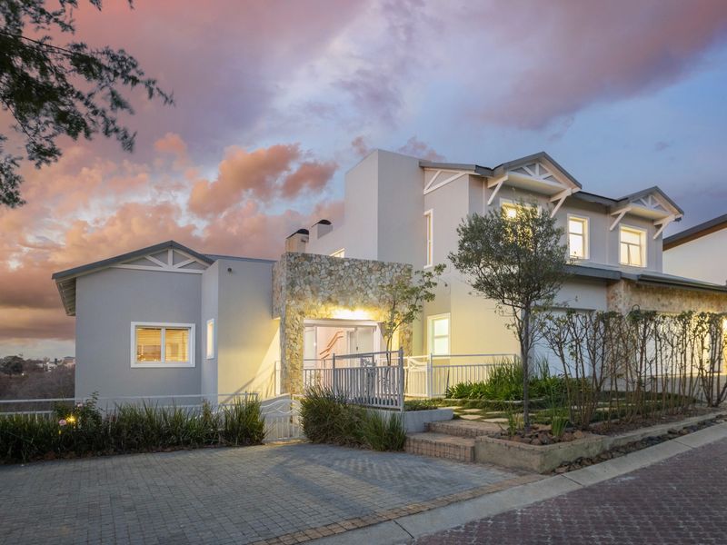 A modern double-story residence featuring stone cladding, a paved driveway, and well-maintained landscaping, captured during a scenic sunset.