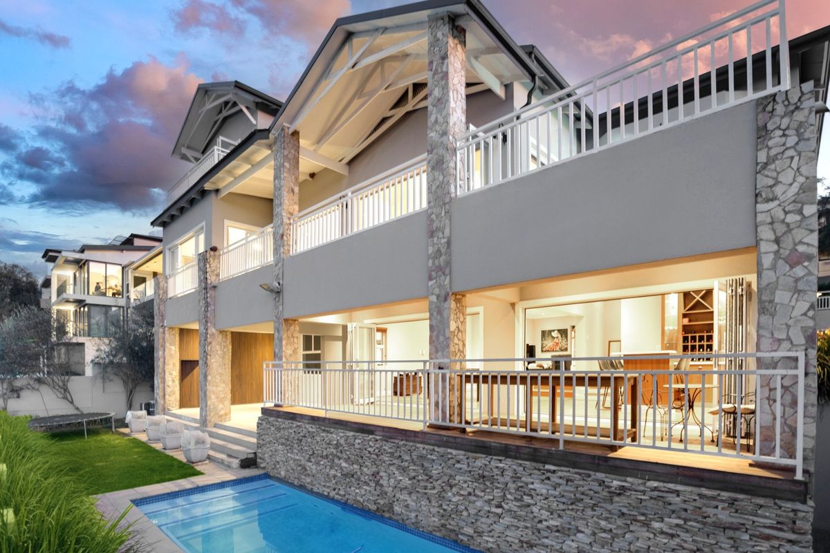 Rear elevation featuring a swimming pool, stone-clad pillars, and a spacious balcony with white railings, offering seamless indoor-outdoor flow through large sliding doors.