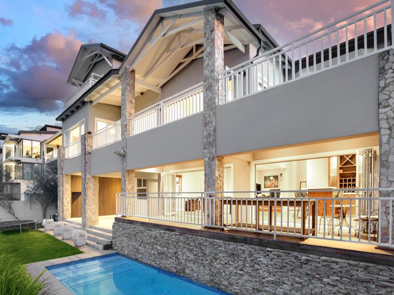 Rear elevation featuring a swimming pool, stone-clad pillars, and a spacious balcony with white railings, offering seamless indoor-outdoor flow through large sliding doors.