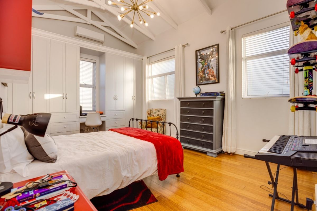 Spacious bedroom featuring vaulted ceilings with exposed rafters, hardwood flooring, extensive built-in cabinetry with an integrated desk, and a split-system air conditioner.
