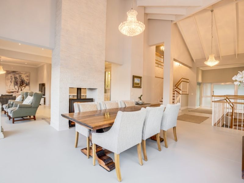 Spacious open-plan living and dining area featuring a vaulted ceiling, exposed beams, a central fireplace, and elegant chandeliers.