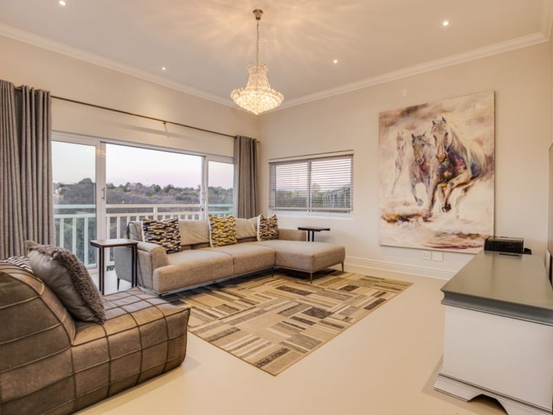 A well-maintained living room featuring recessed lighting, a crystal chandelier, and large sliding glass doors that open to a balcony with scenic views.