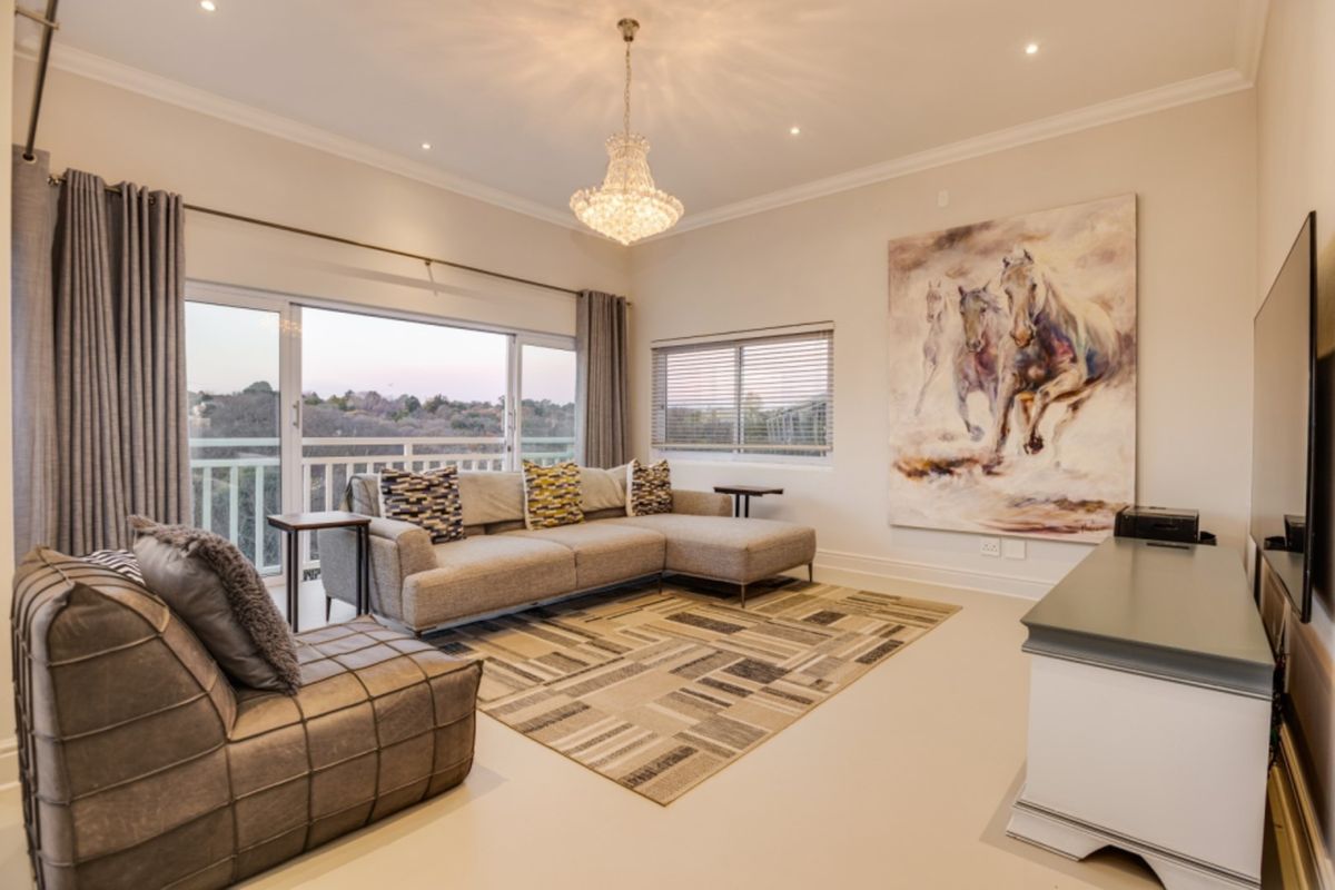 A well-maintained living room featuring recessed lighting, a crystal chandelier, and large sliding glass doors that open to a balcony with scenic views.