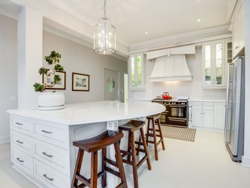 A bright, modern kitchen featuring a large central island with quartz countertops, custom white cabinetry, and a professional-style range cooker.
