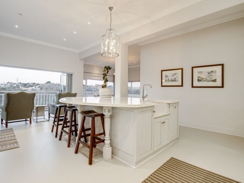 Bright open-plan kitchen area featuring a central island with an apron sink, flowing seamlessly onto a balcony with scenic views.