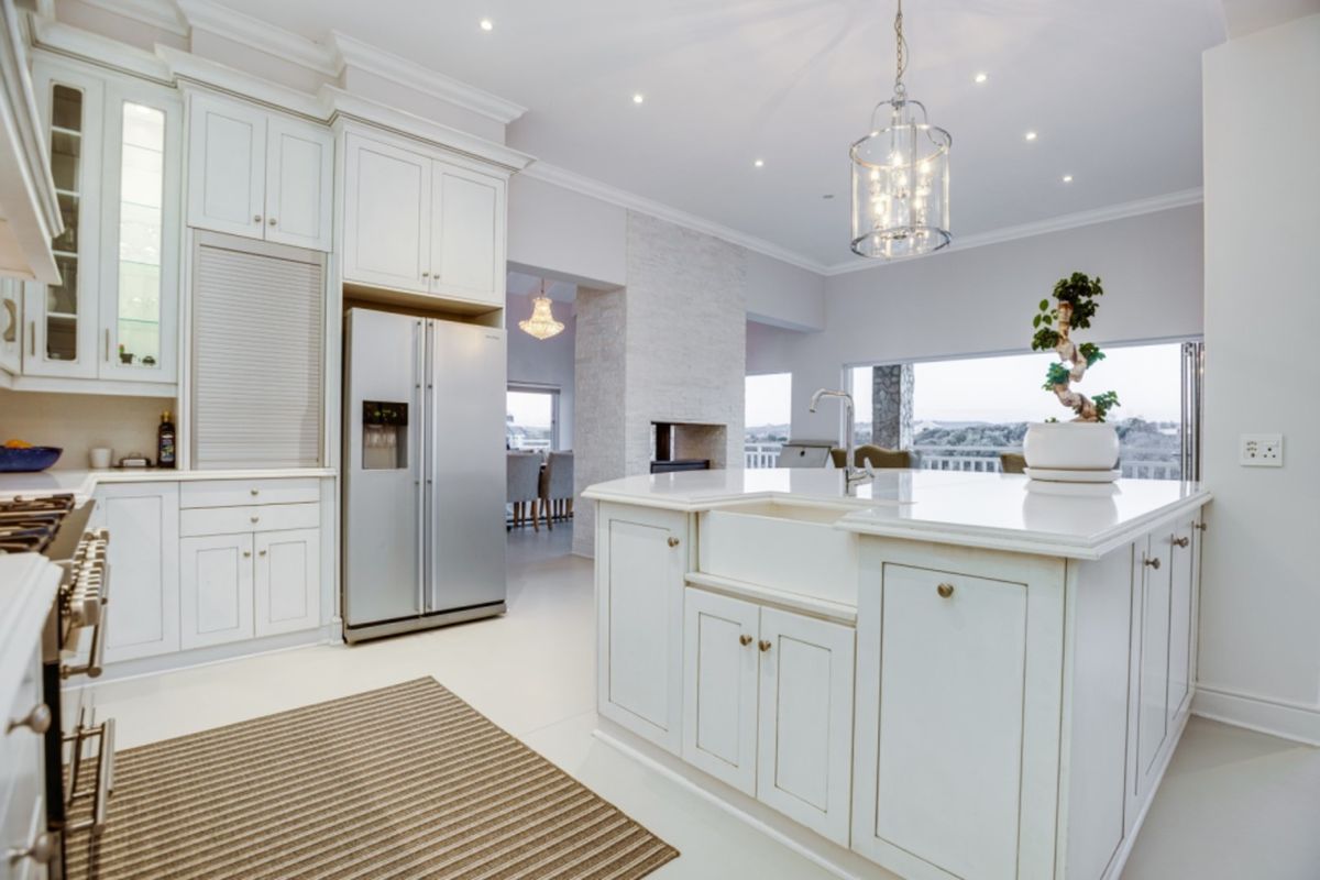 A bright, modern kitchen featuring white cabinetry, a large central island with a farmhouse sink, stone countertops, and integrated appliances.
