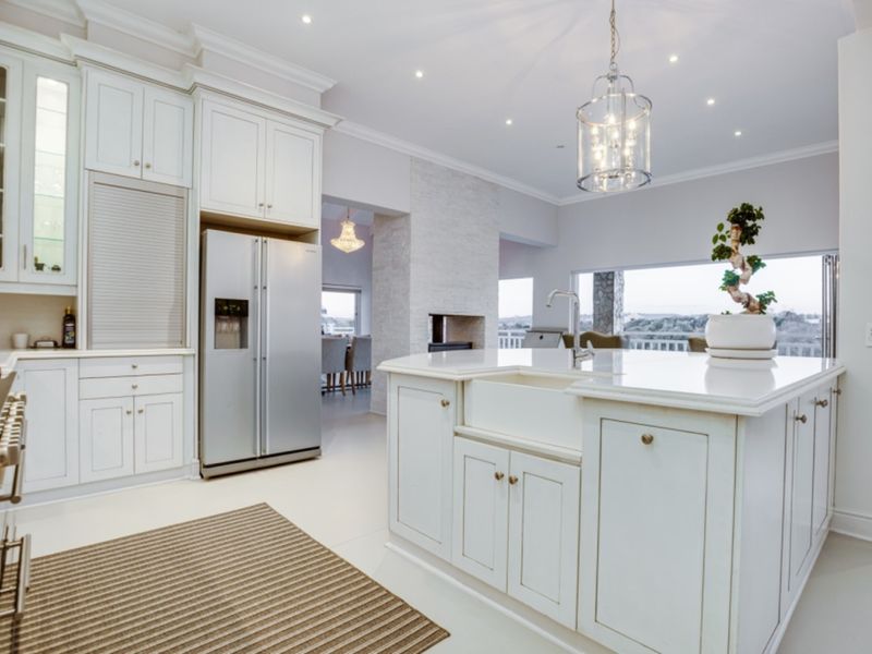 A bright, modern kitchen featuring white cabinetry, a large central island with a farmhouse sink, stone countertops, and integrated appliances.
