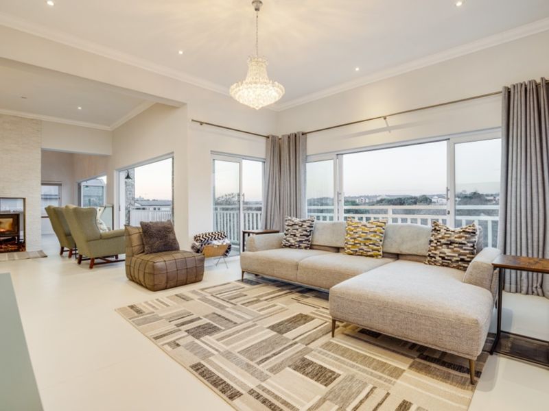 Spacious open-plan living area featuring a modern wood-burning fireplace, elegant crystal chandelier, and large sliding glass doors leading to an outdoor balcony.