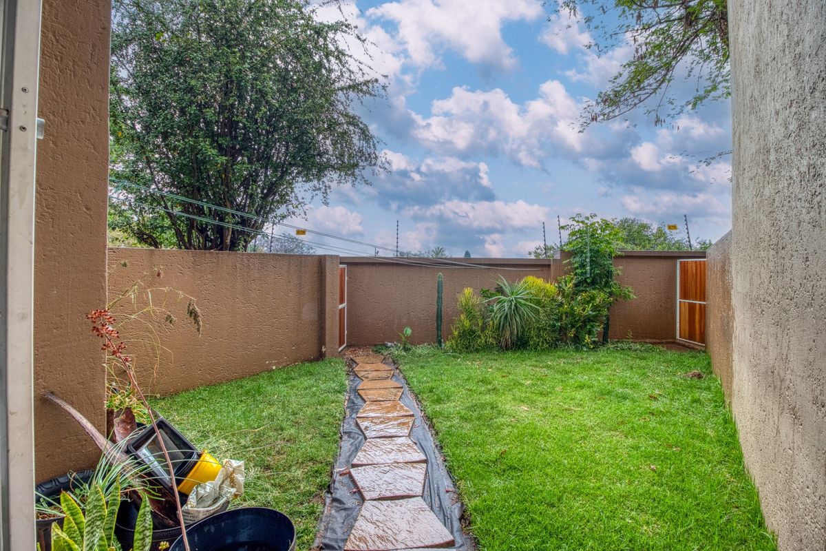 A private rear garden area featuring a lawn, a stone pathway, and high boundary walls with integrated electric fencing.