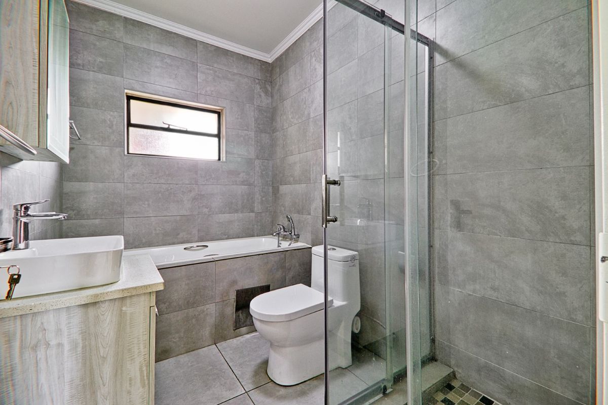 Modern bathroom featuring grey wall and floor tiles, a glass-enclosed shower, a built-in bathtub, and a contemporary vanity with a vessel sink.